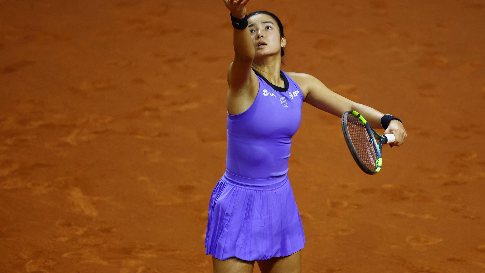 Alexandra Eala in a purple tennis outfit tossing a ball for a serve