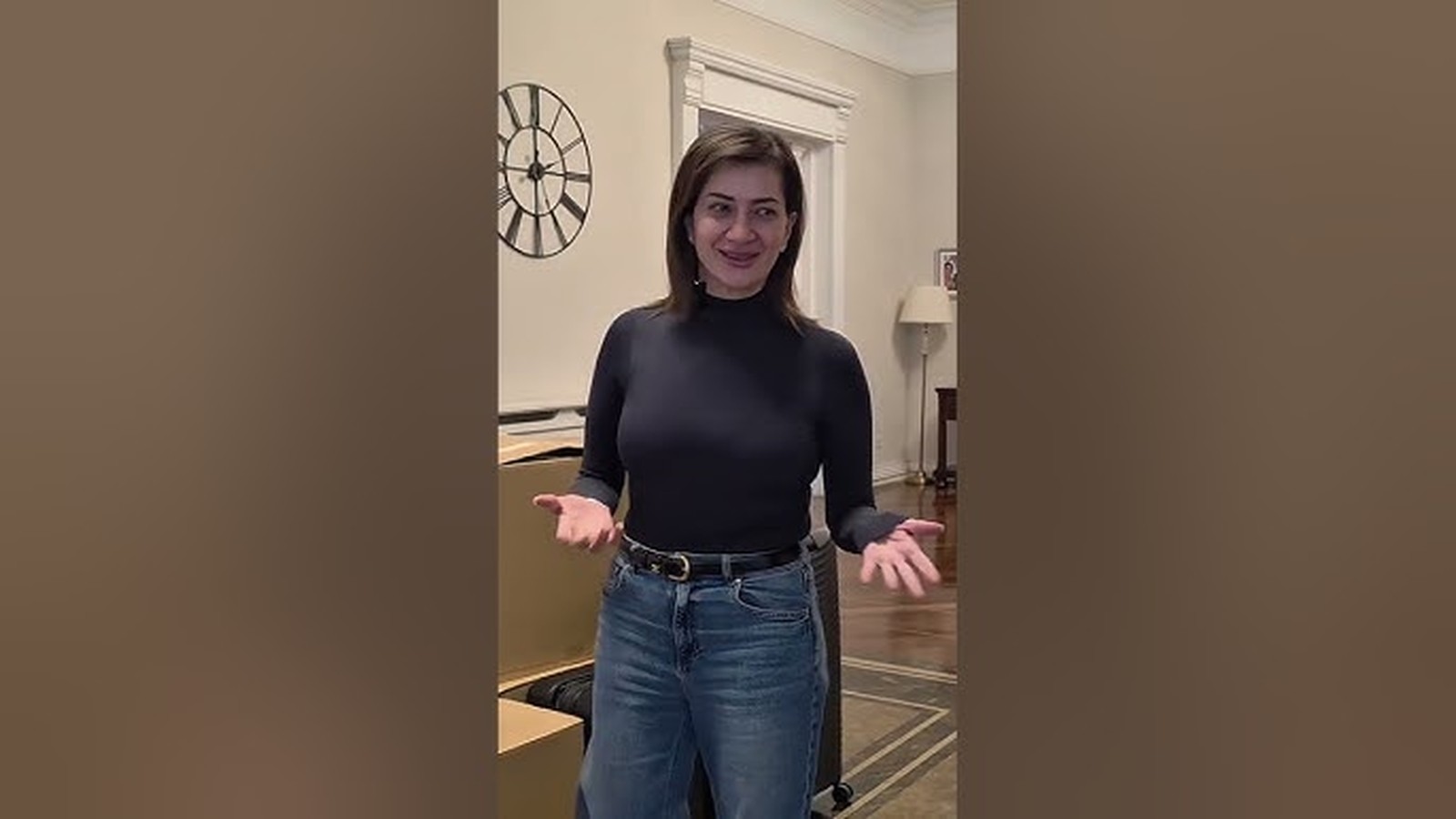 Anna Hakobyan standing in a room with cardboard boxes and a wall clock