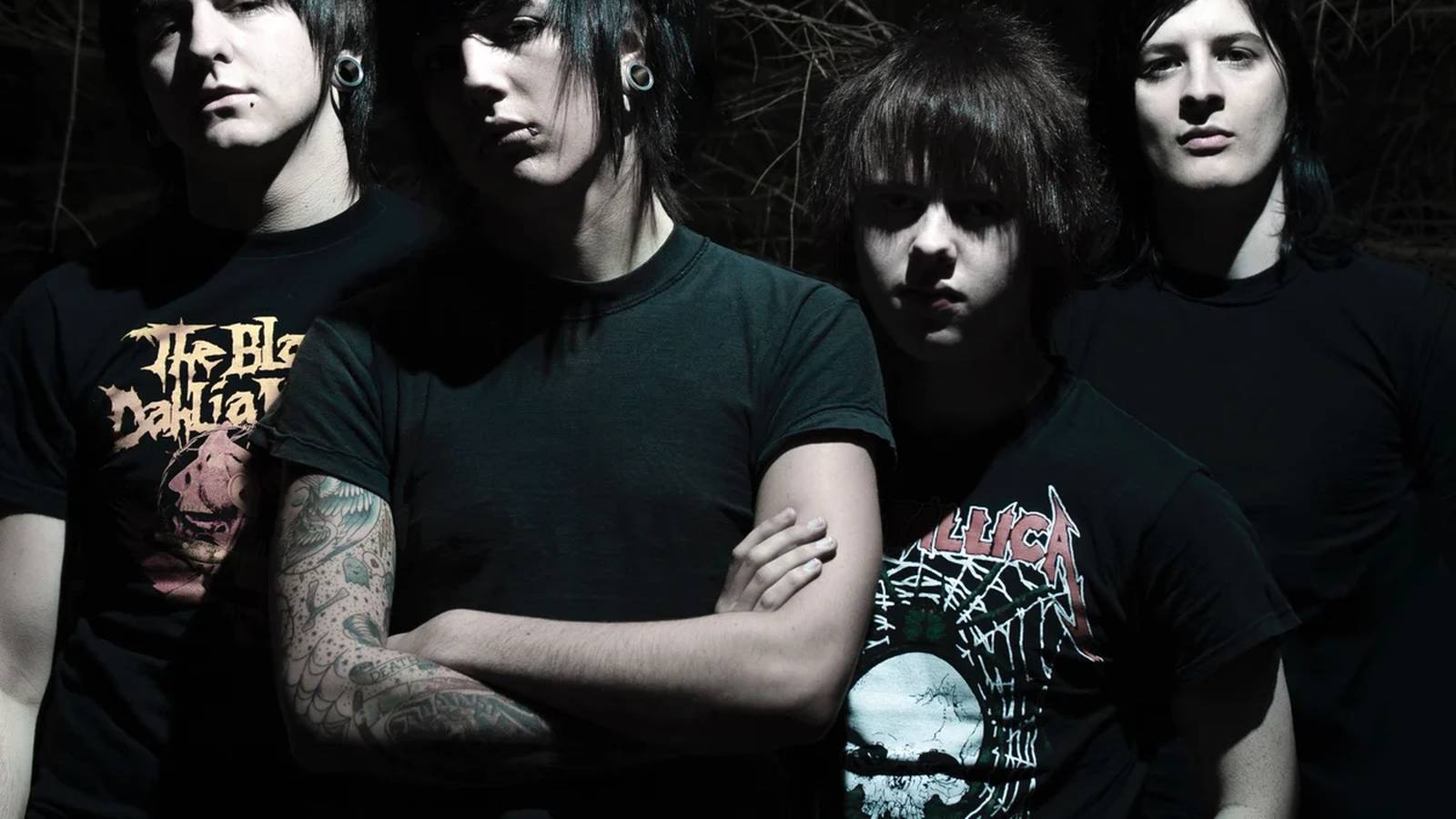 Four young band members with emo hairstyles posing against a dark background