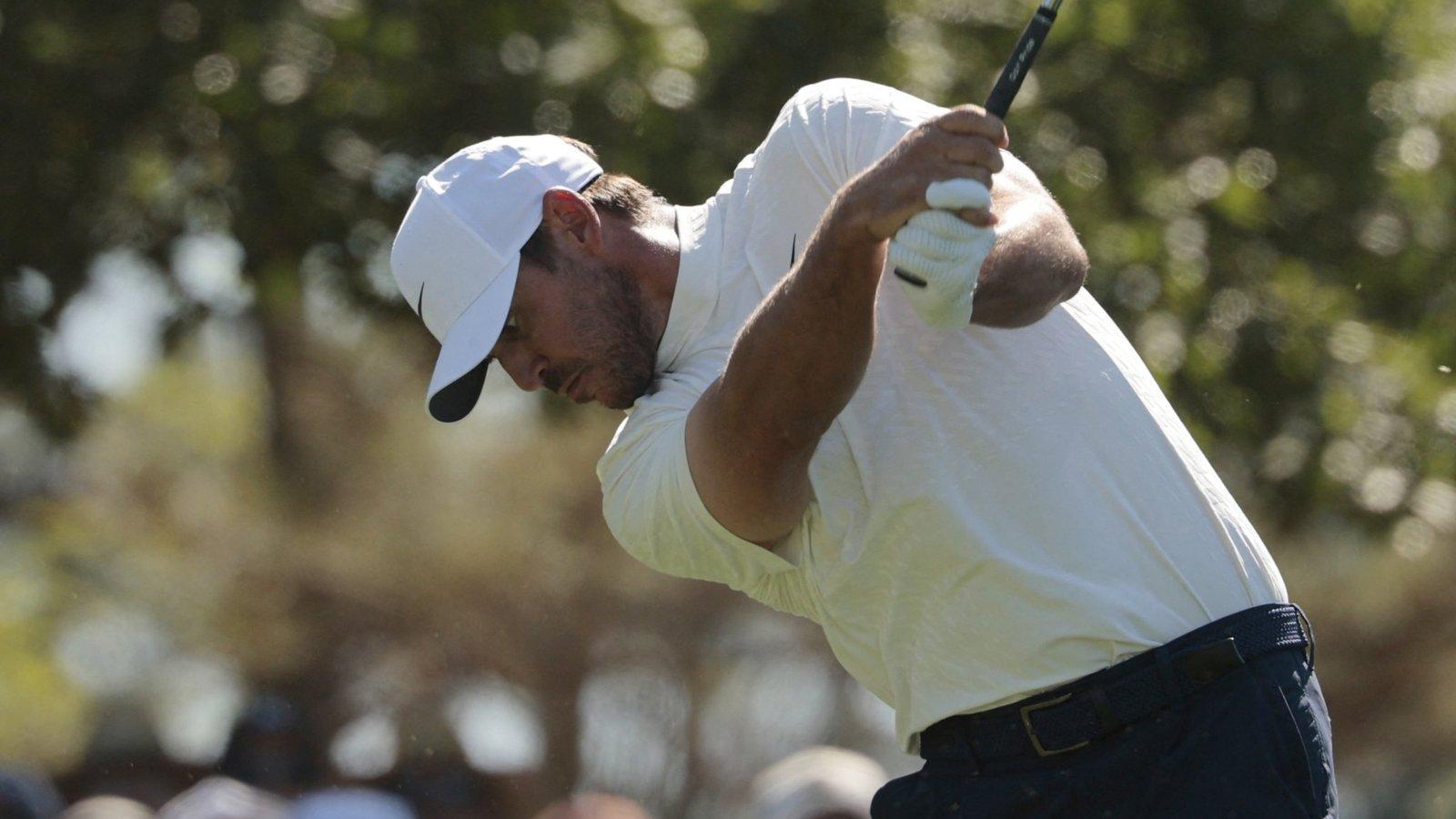 Brooks Koepka wearing a white hat and shirt performing a powerful golf swing
