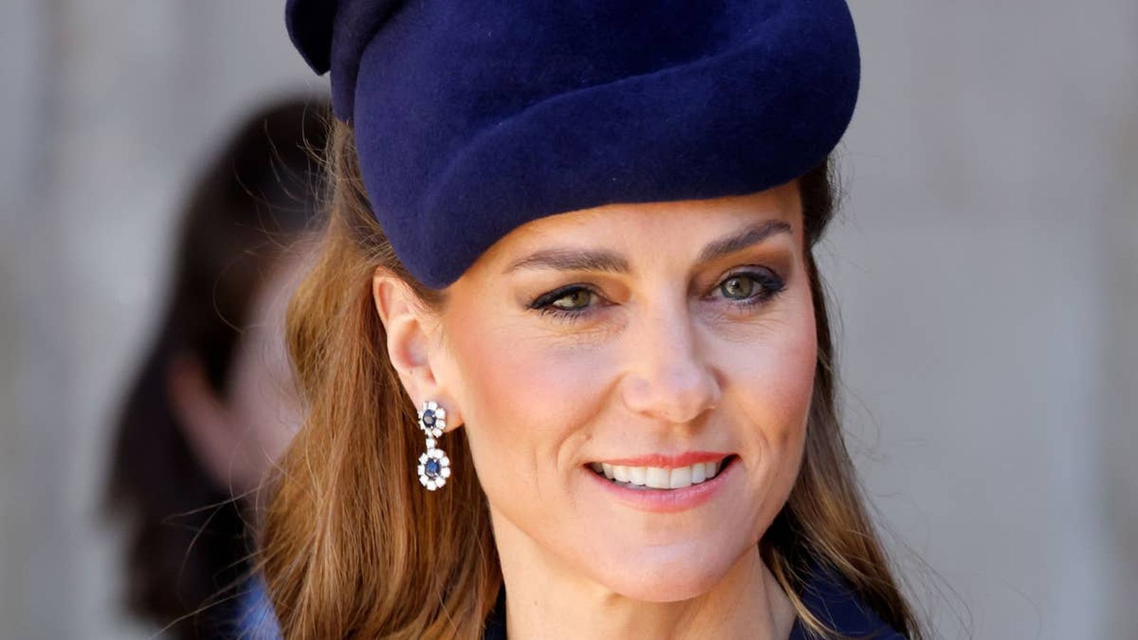 Close up portrait of Catherine, Princess of Wales wearing a navy hat and earrings.