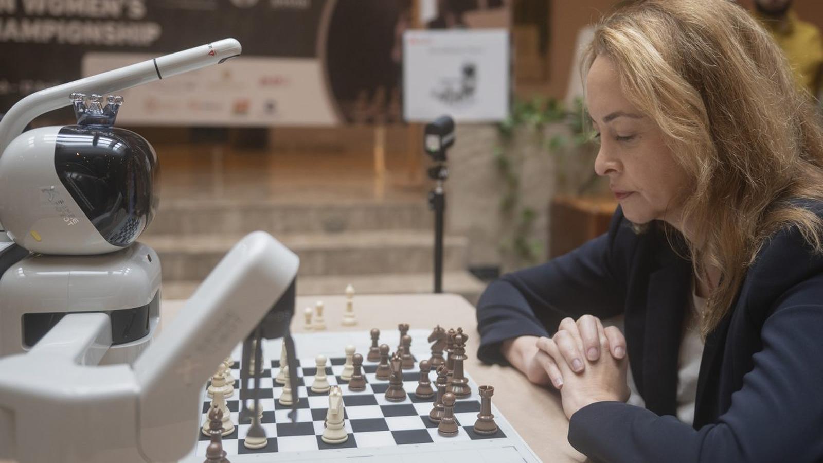 A woman playing a chess match against a robotic arm on a board