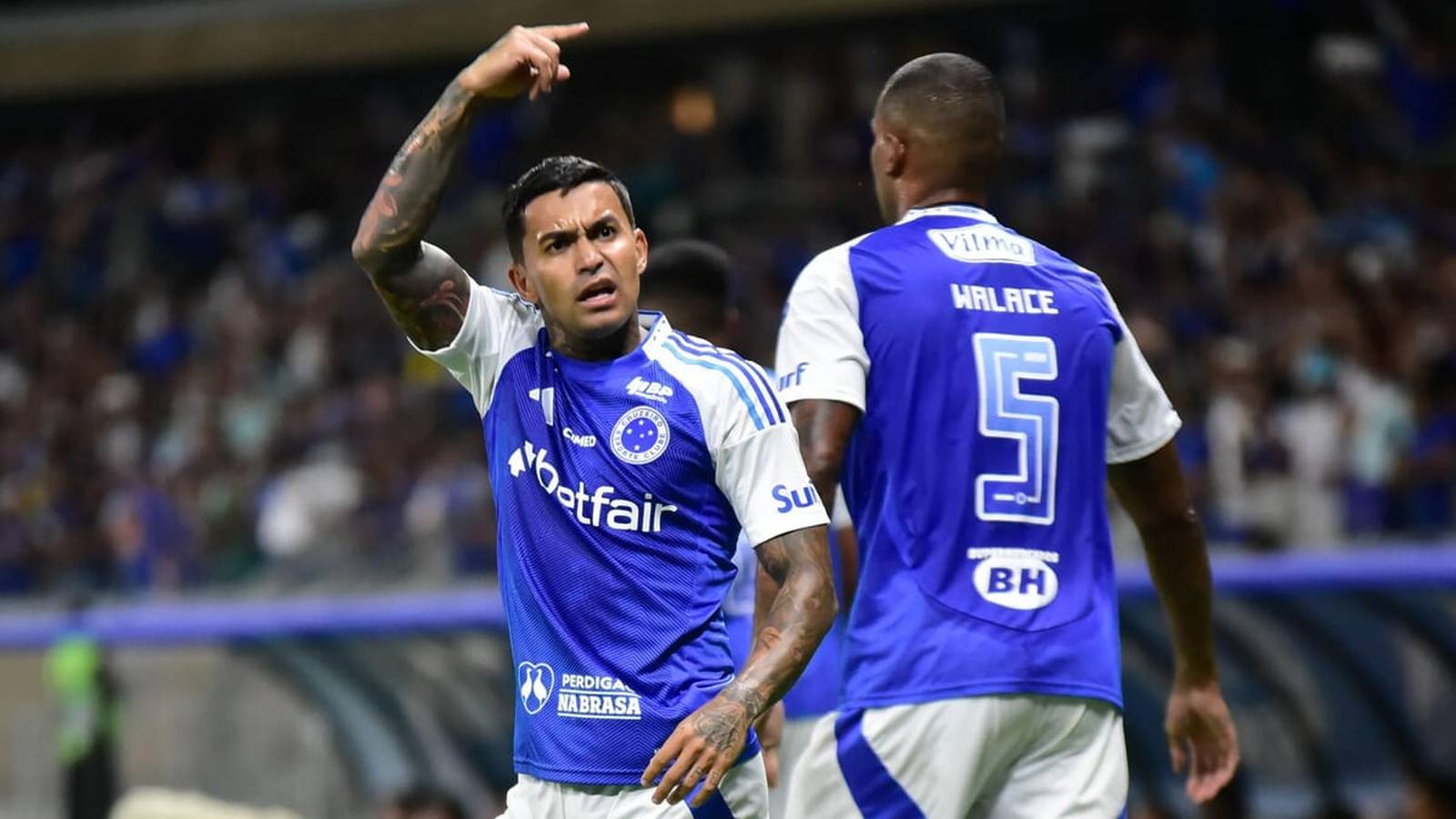 Cruzeiro player in blue jersey celebrates, pointing upwards with teammate nearby