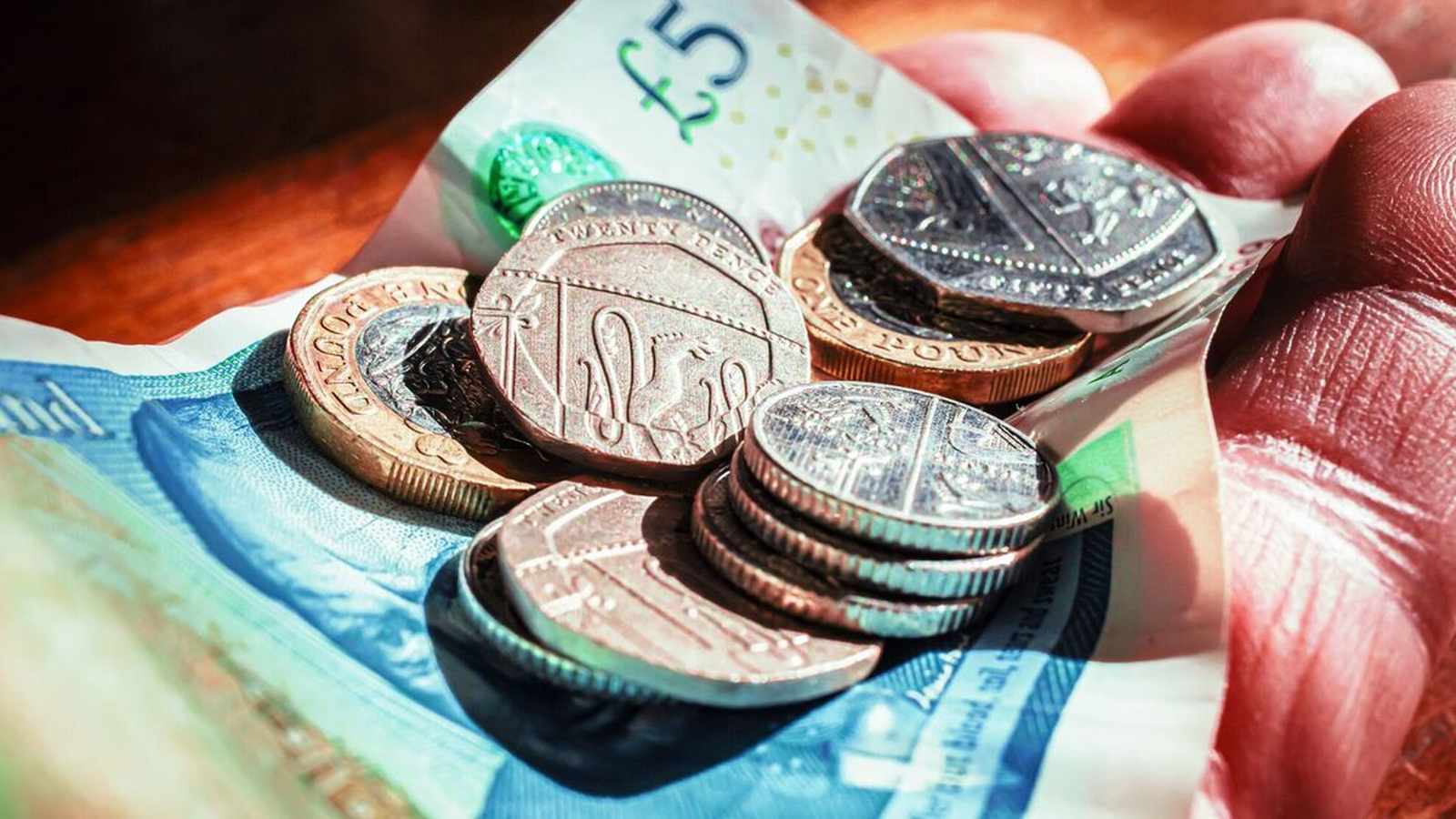 A close-up of a person holding British pound coins and banknotes in their hand.