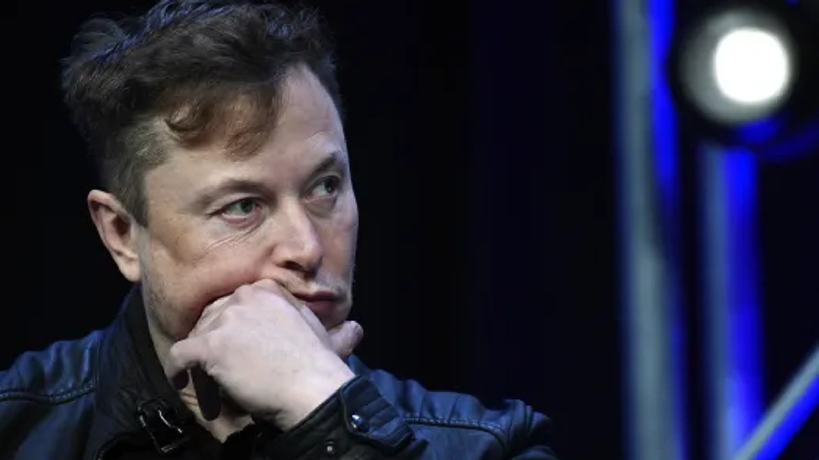 Elon Musk resting his chin on his hand while looking off to side