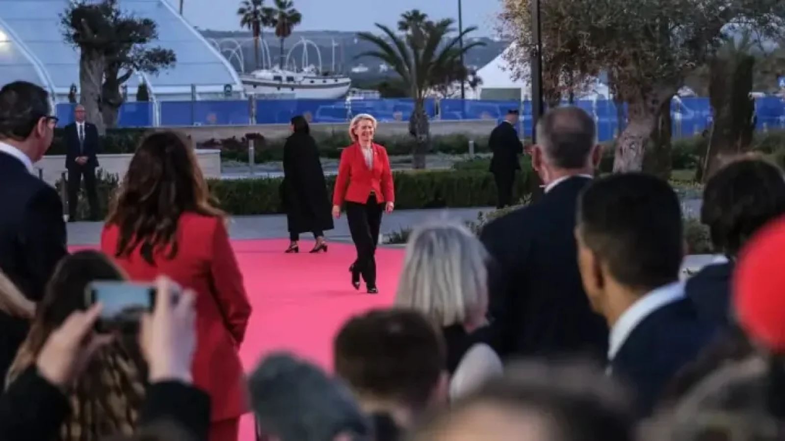 Ursula von der Leyen walks on a red carpet surrounded by officials