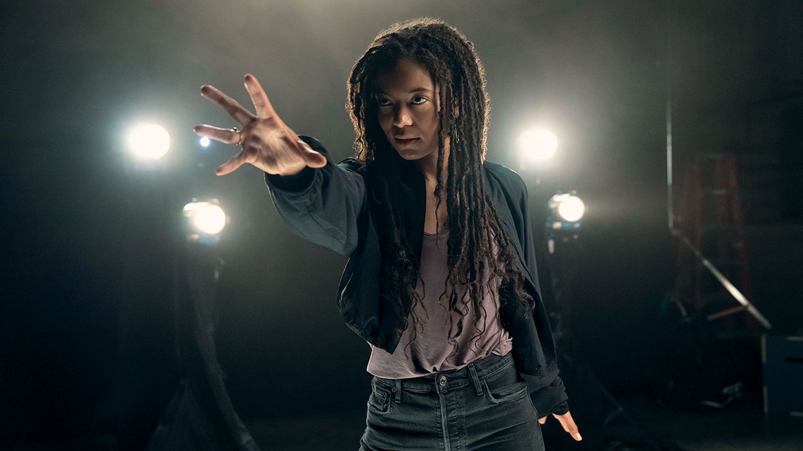 Marie Moreau reaches out with her hand in a dramatic studio setting