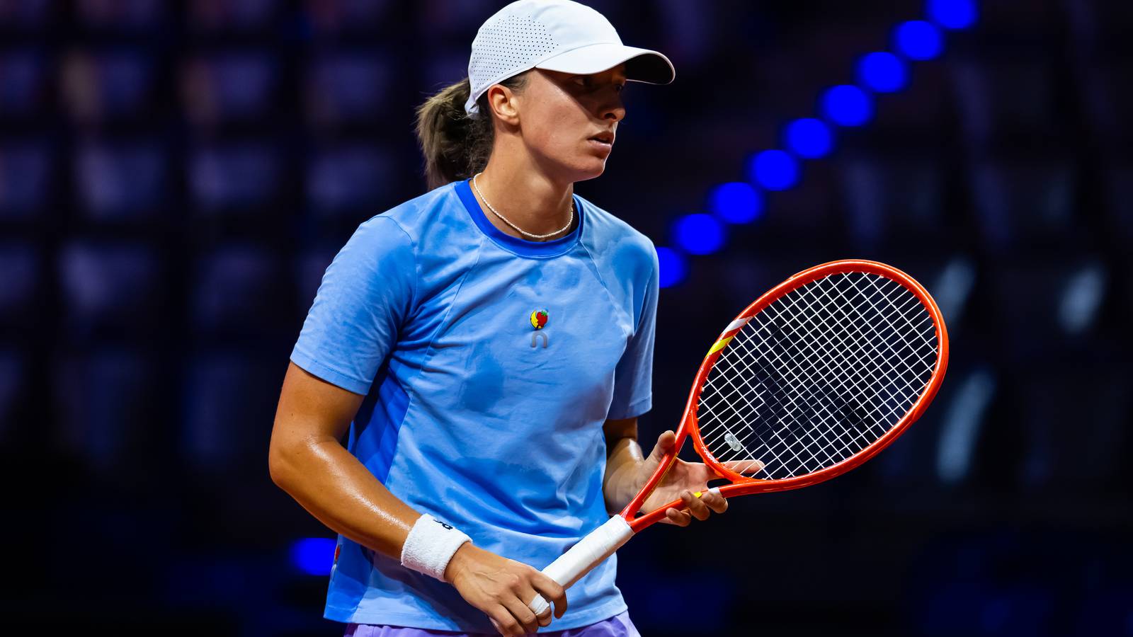 Iga Swiatek wearing a white cap and blue shirt holding a tennis racket