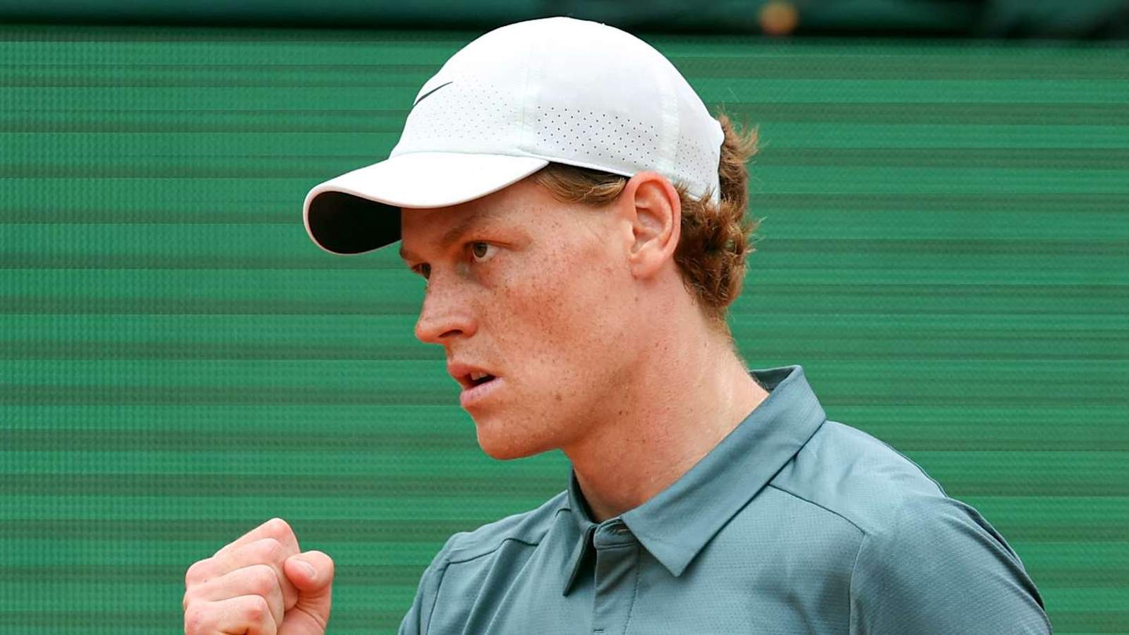 Jannik Sinner wearing a white cap clenches his fist during a tennis match