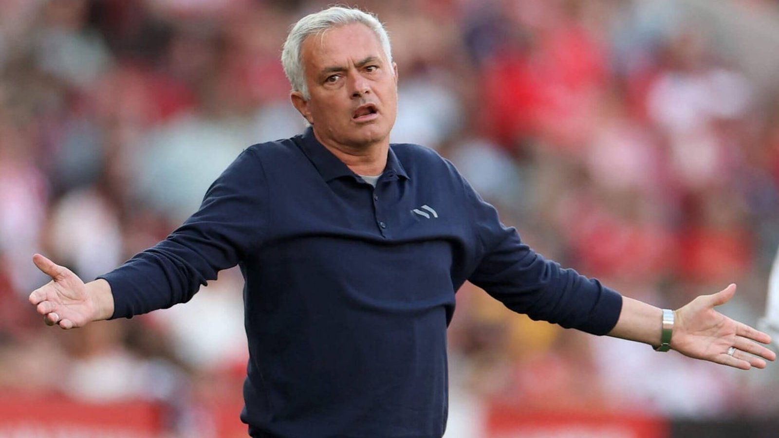 Jose Mourinho standing on the pitch with arms outstretched in a frustrated gesture