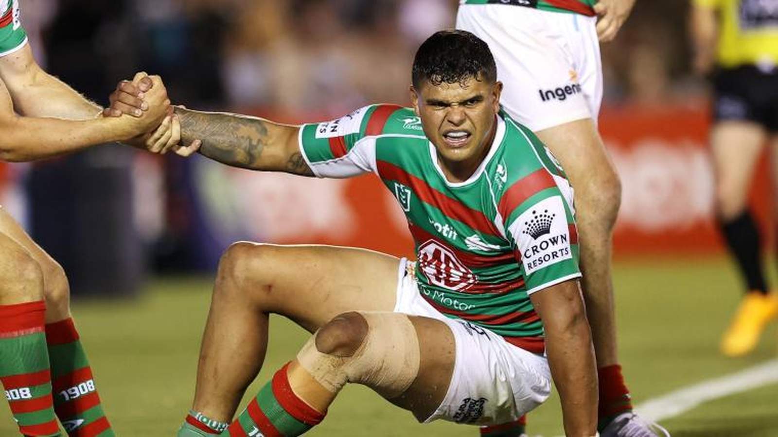Latrell Mitchell grimacing in pain while sitting on the field during a match