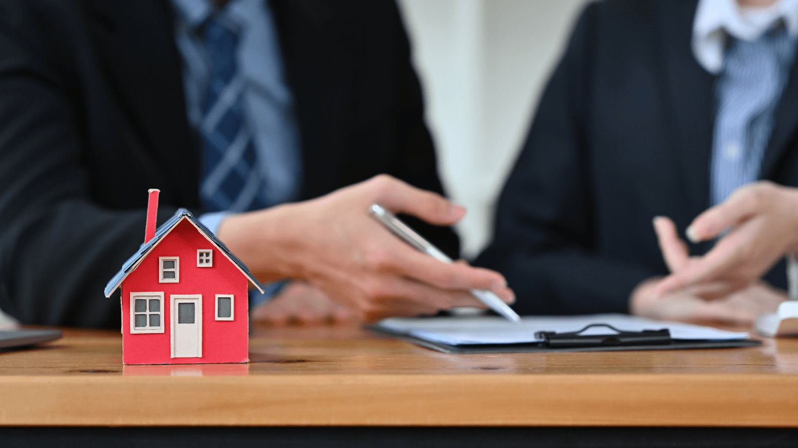 A small red house model sits on a desk during a mortgage consultation