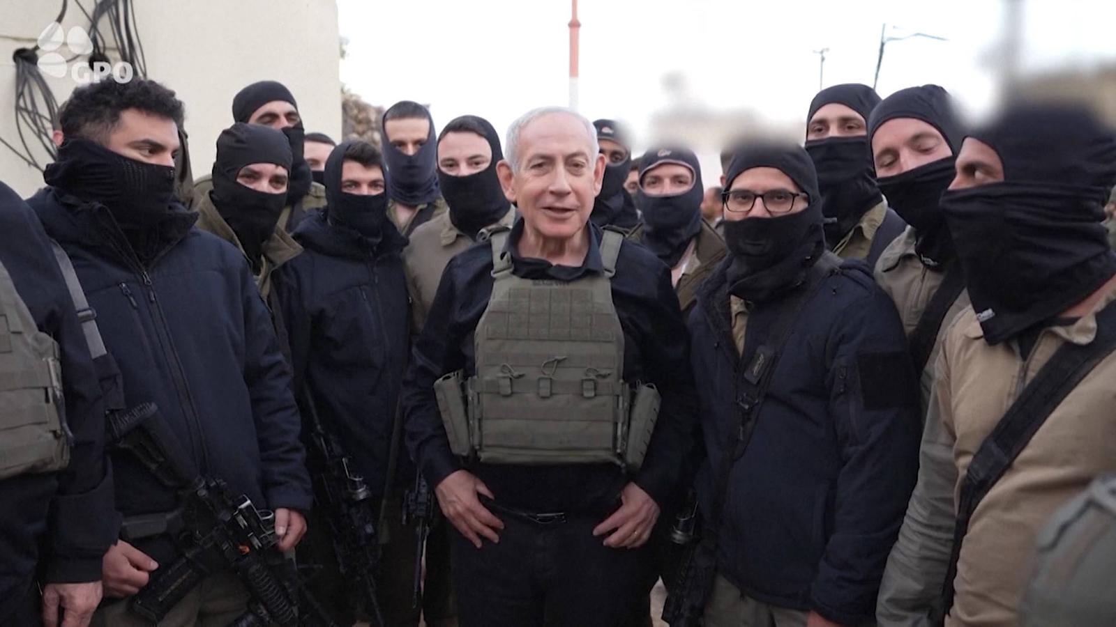 Benjamin Netanyahu wearing a tactical vest surrounded by masked Israeli soldiers in uniform