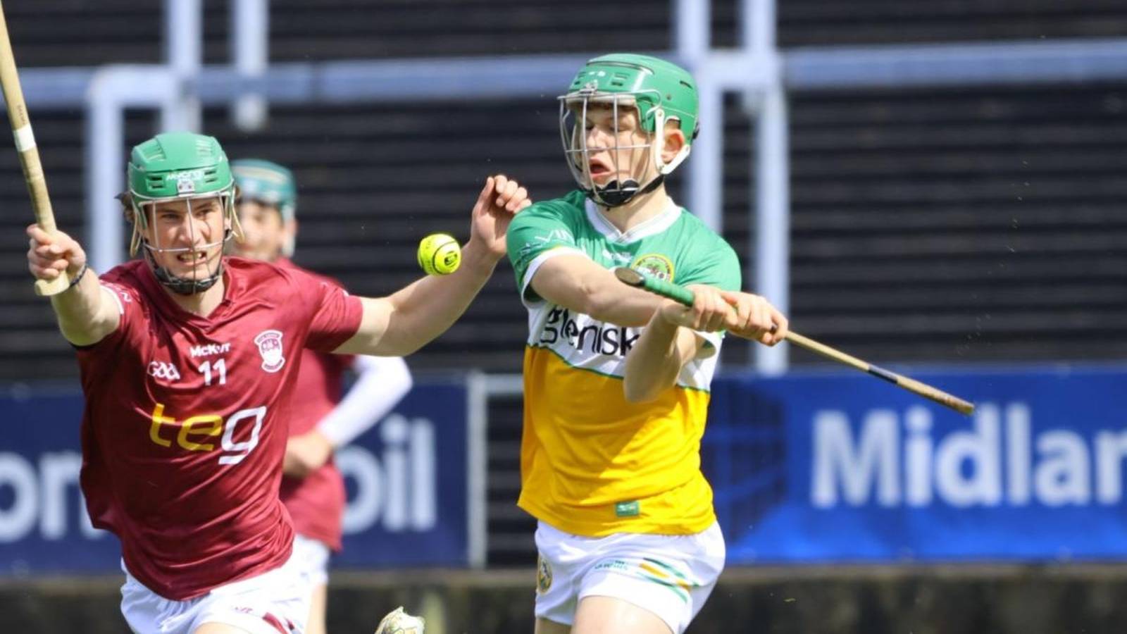 A young hurler in green and yellow jersey swings his stick during match