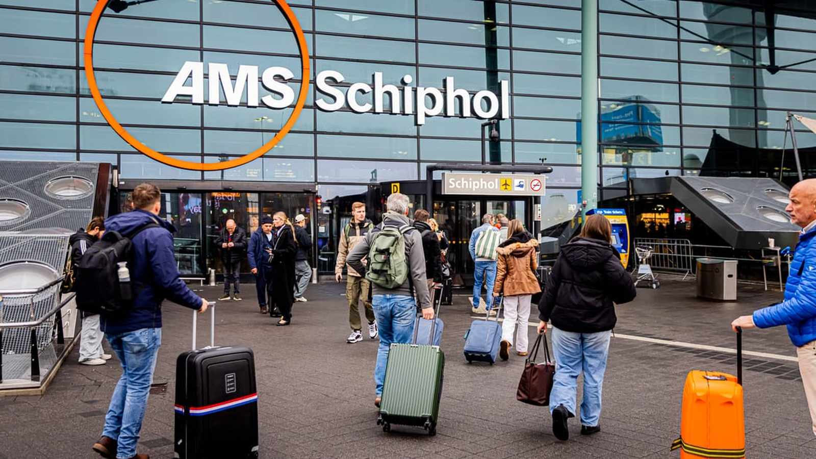 Travelers with luggage walking outside the entrance of Amsterdam Schiphol Airport terminal building