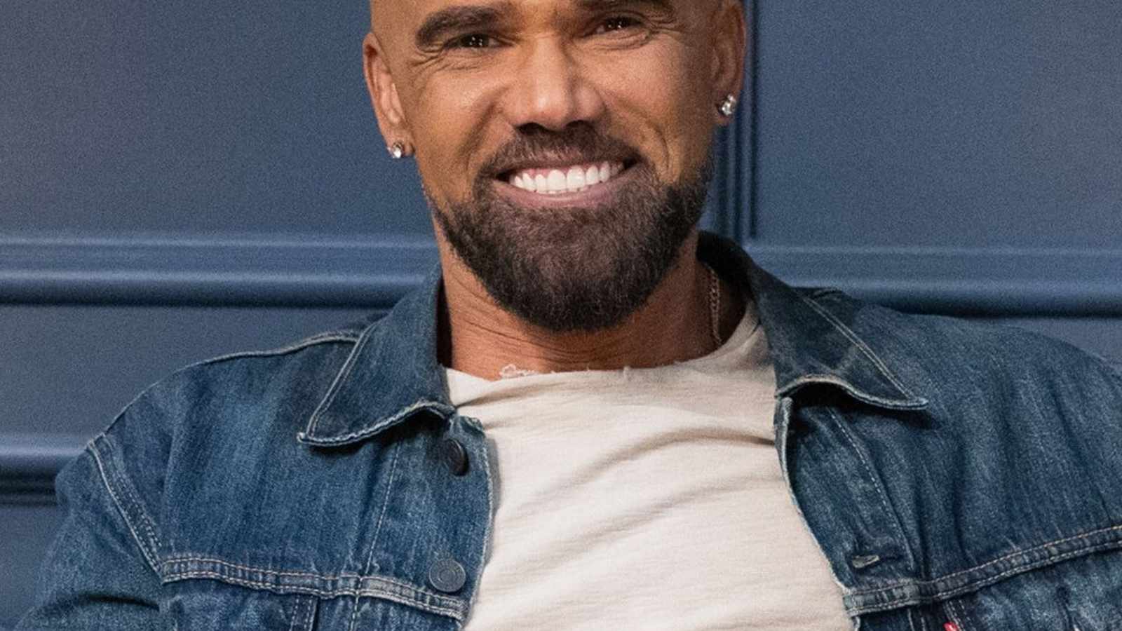 Actor Shemar Moore smiling while wearing a denim jacket against a blue background