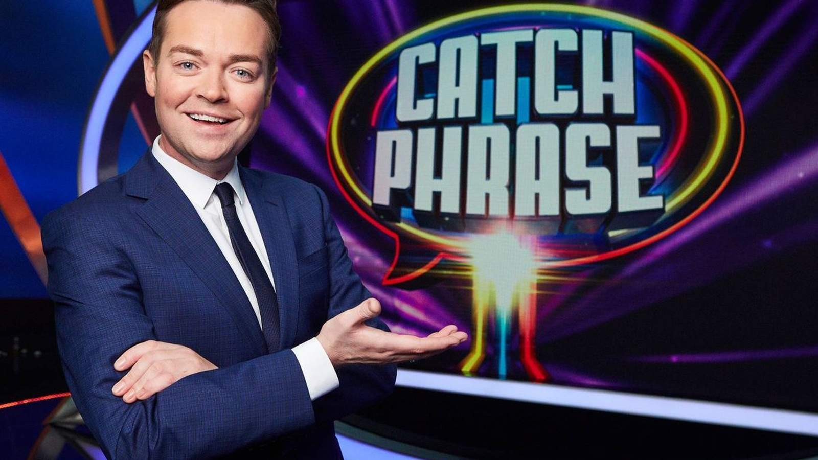 Television presenter Stephen Mulhern smiling in a suit in front of the Catchphrase logo