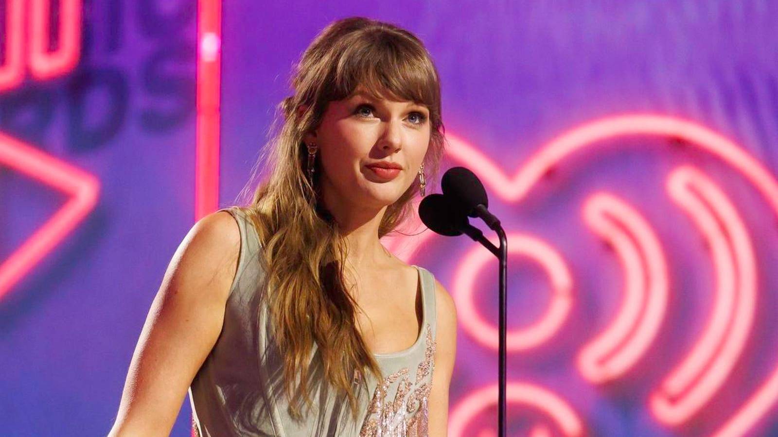 Taylor Swift speaking into a microphone at an awards ceremony with neon lighting
