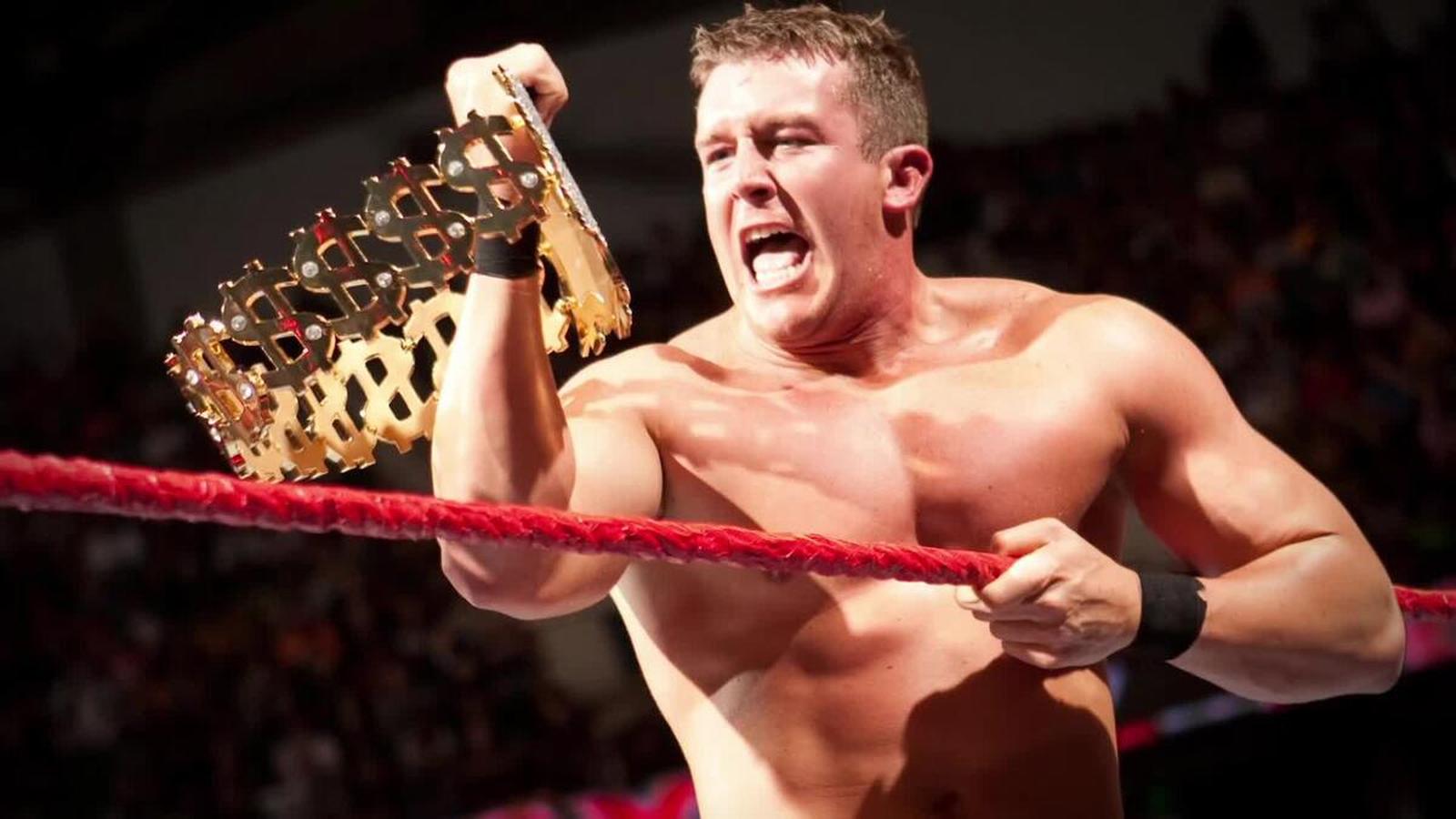 Ted DiBiase Jr. shouting while holding a gold championship belt in a wrestling ring.