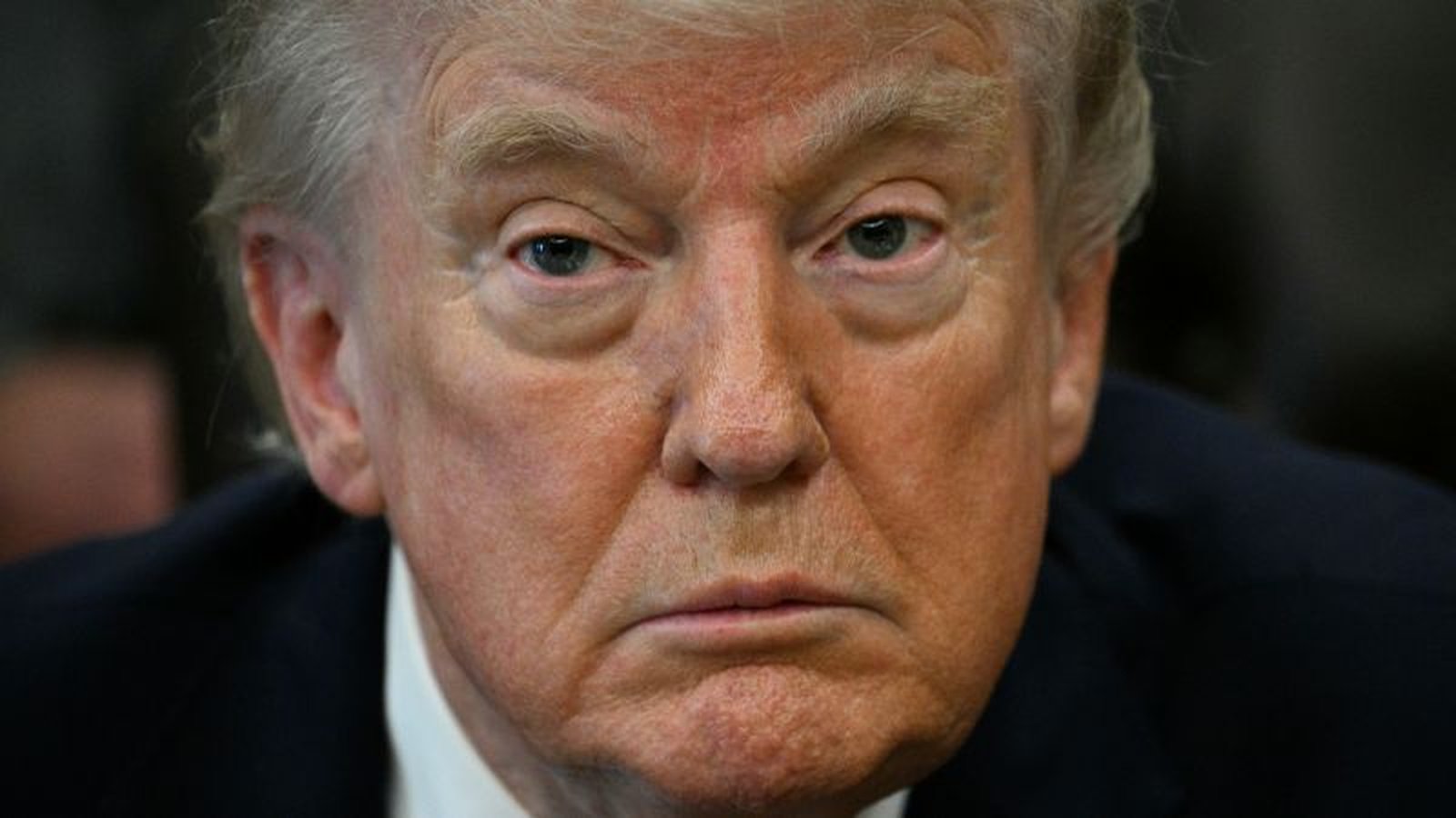A close-up portrait of Donald Trump looking directly at the camera with a serious expression.