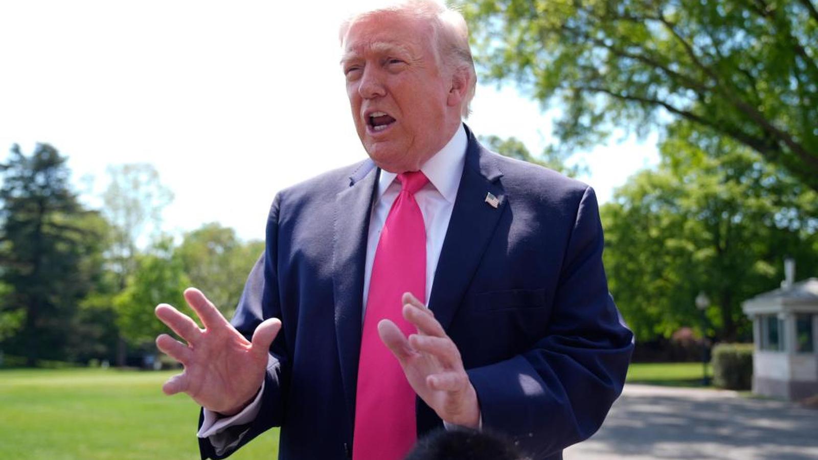 Donald Trump speaking outdoors while wearing a navy blue suit and pink tie