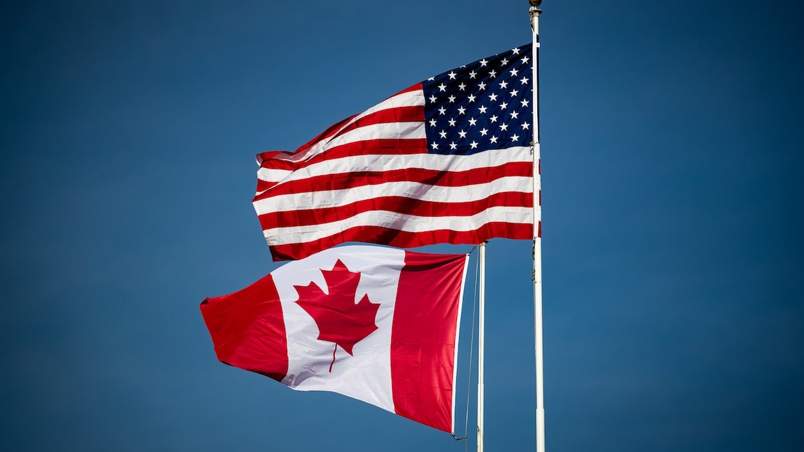The national flags of the United States and Canada flying against a clear blue sky.