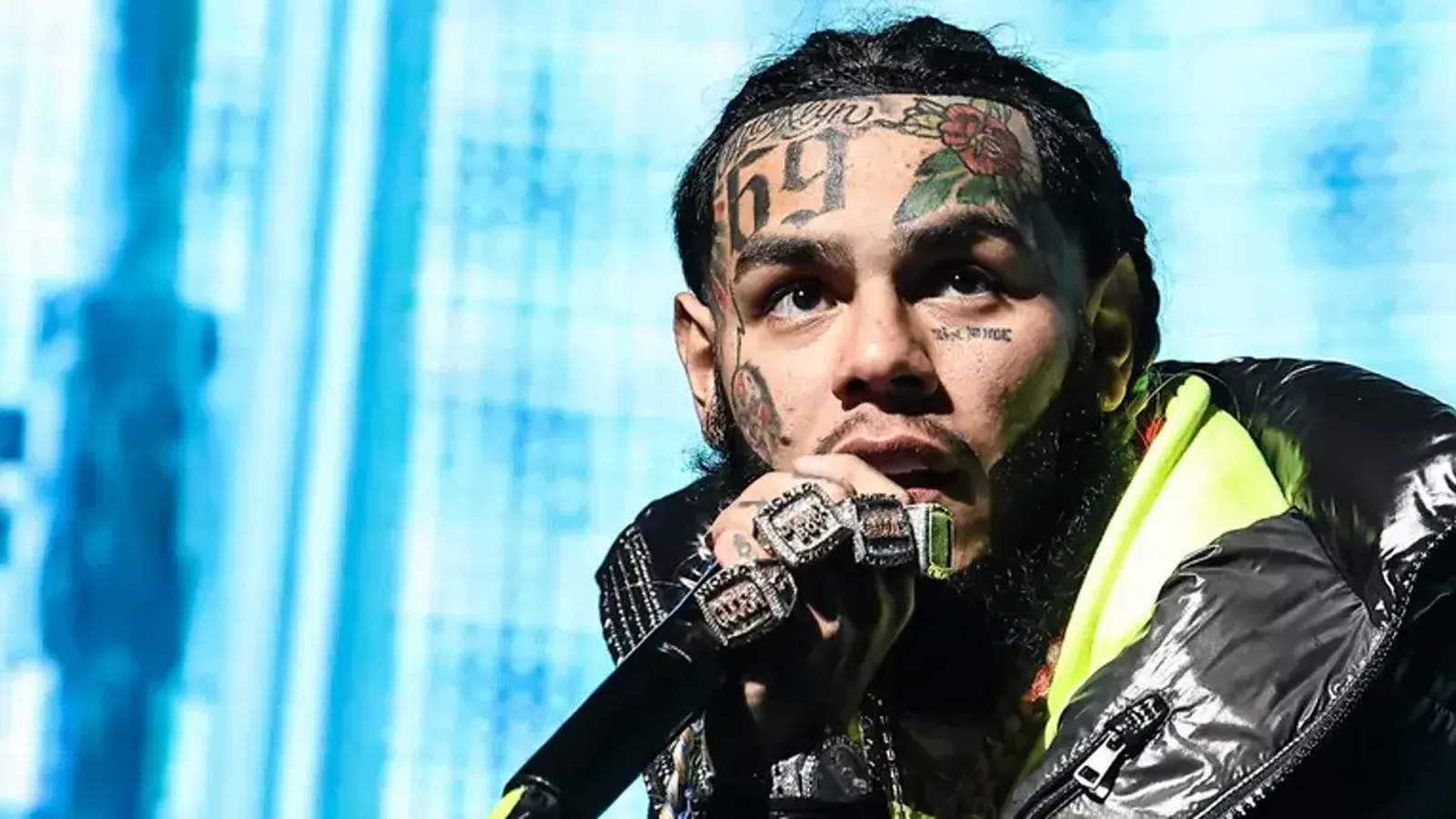 Rapper 6ix9ine with facial tattoos performing on stage while holding a microphone