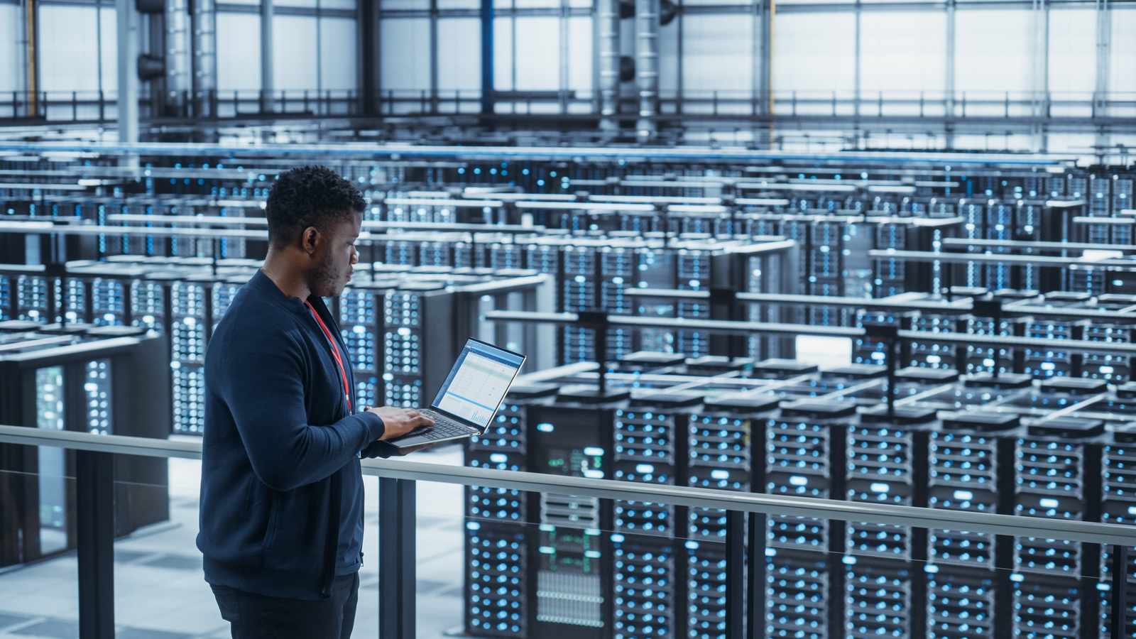A technician using a laptop to monitor servers in a large data center facility