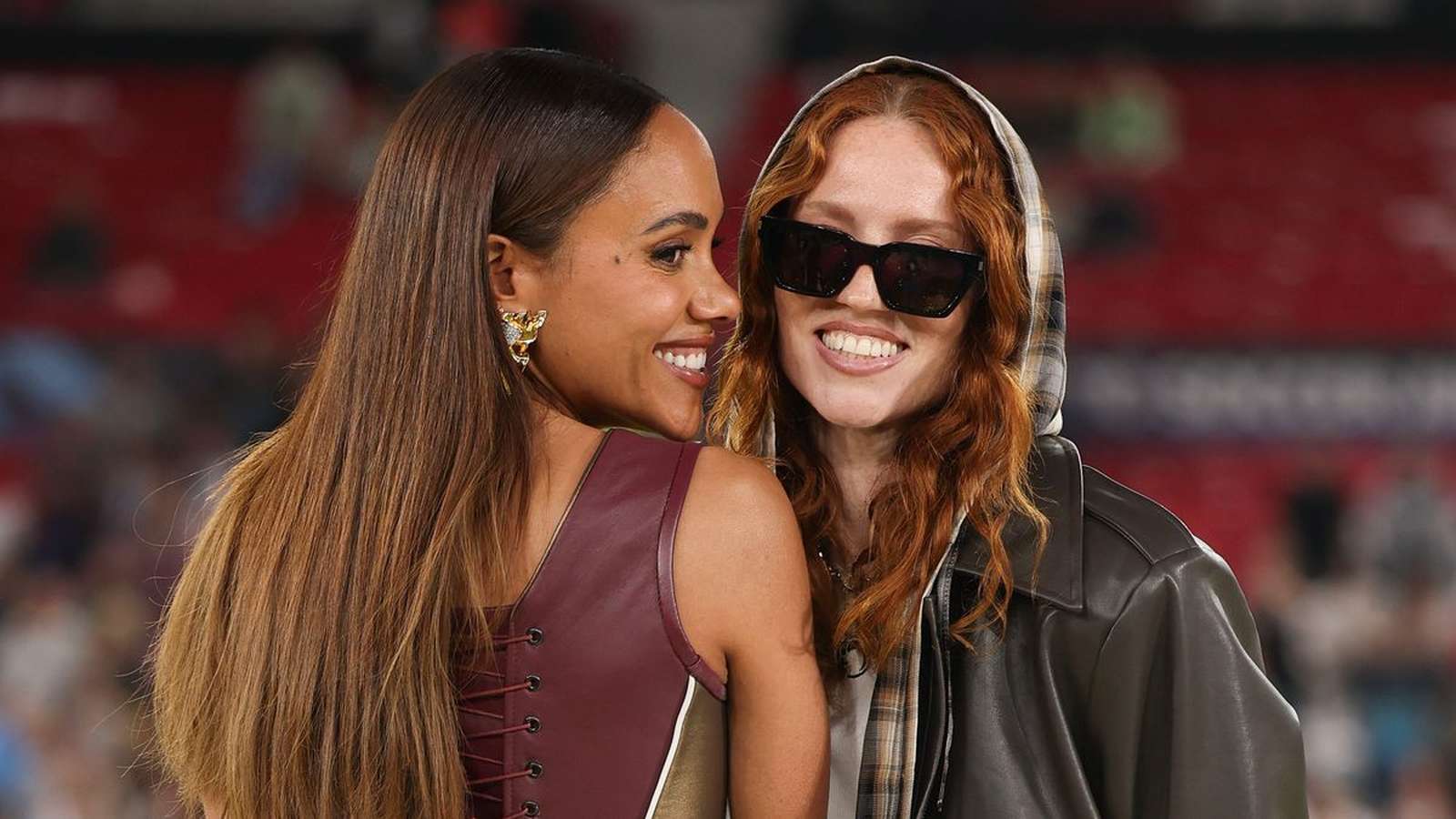 Alex Scott smiling while standing next to a person wearing sunglasses and hoodie