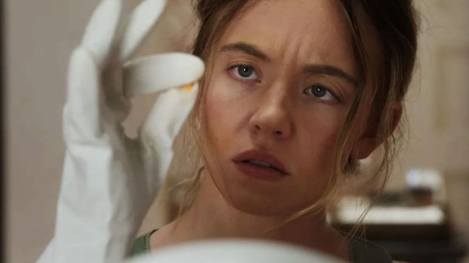 Amanda Seyfried wearing white gloves while examining a small pill in a scene