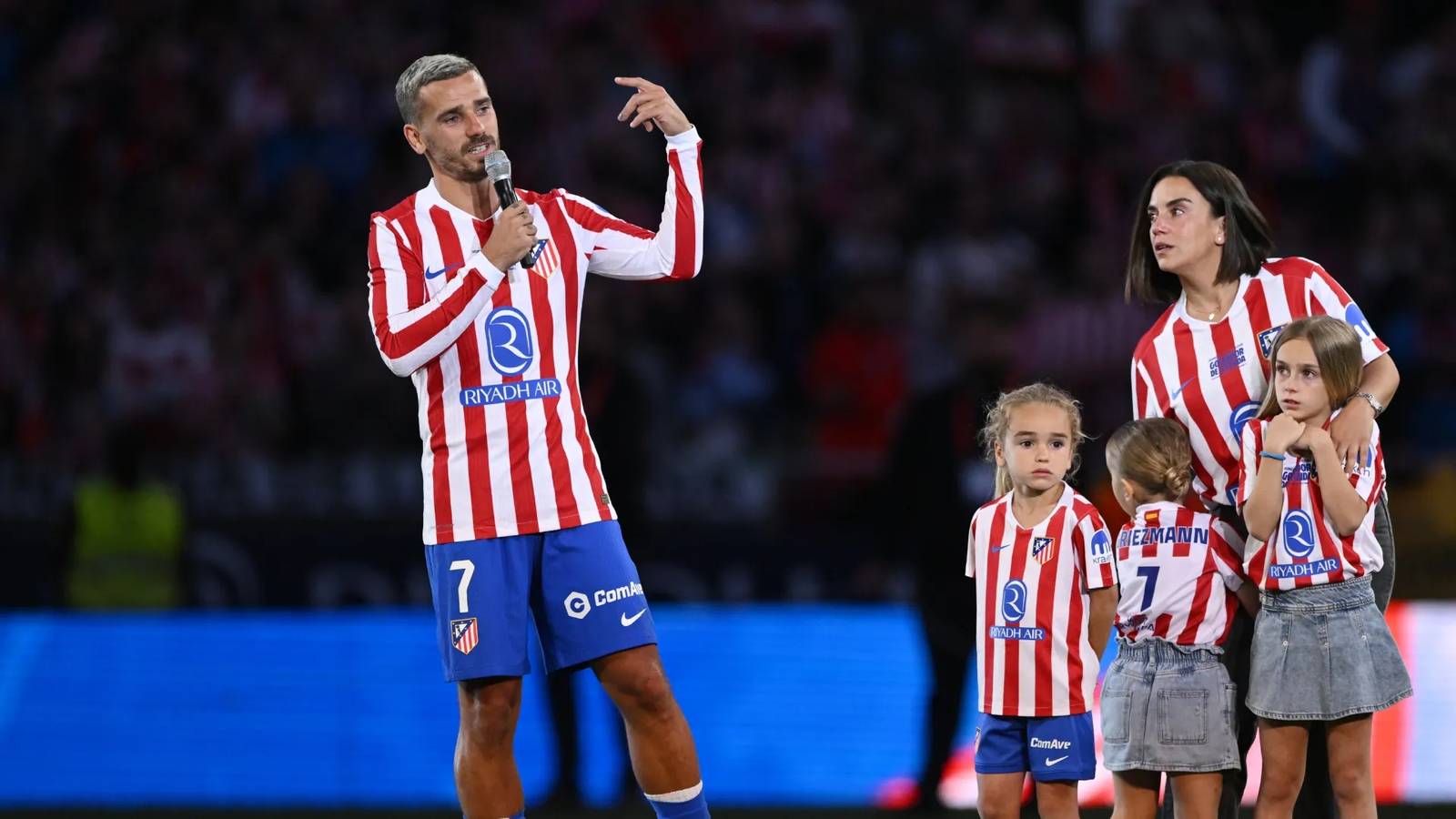 Antoine Griezmann speaking into a microphone on the pitch with his family nearby