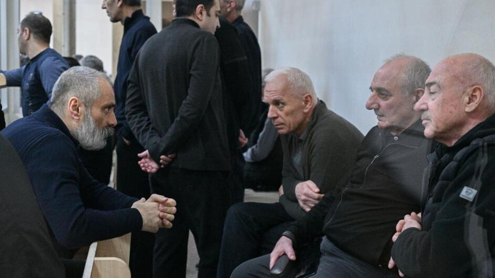 Several Armenian men sitting in a courtroom setting behind a glass partition