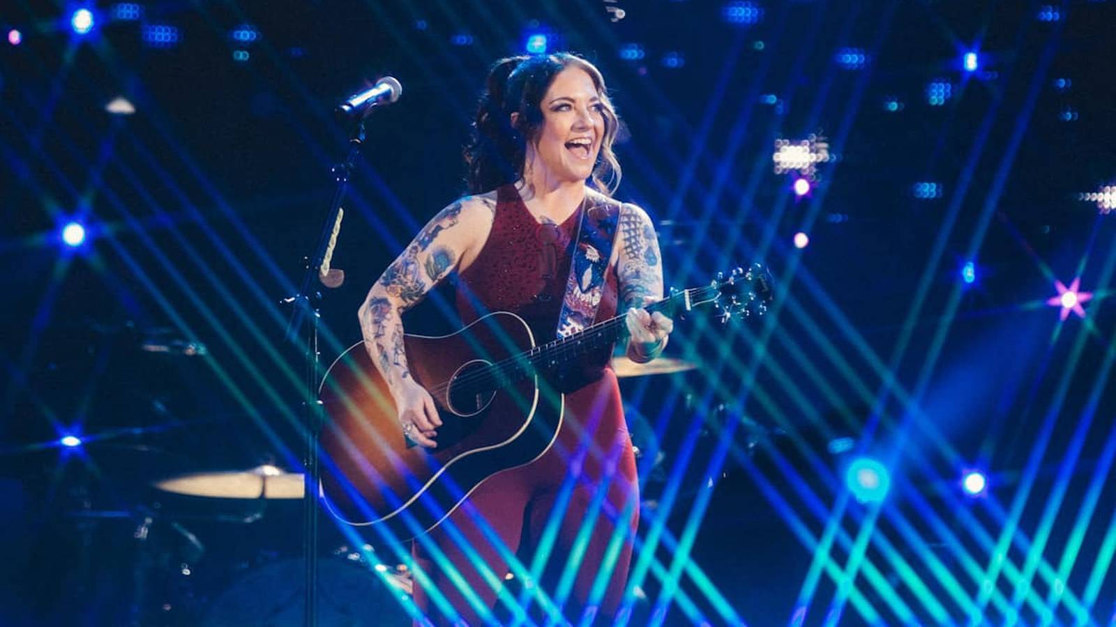 Ashley McBryde singing and playing acoustic guitar on a brightly lit stage