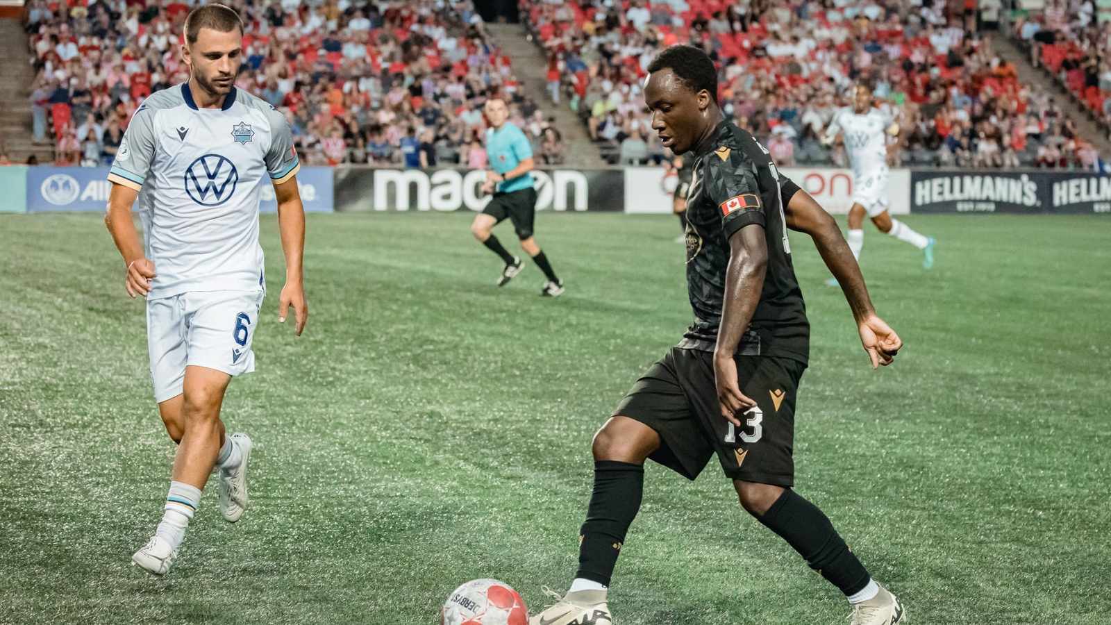 Atlético Ottawa player in black jersey dribbling ball against opponent in white jersey