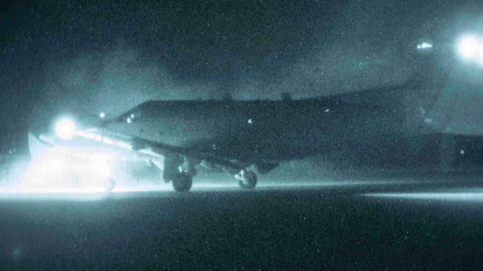A military aircraft parked on an airfield tarmac under bright floodlights at night