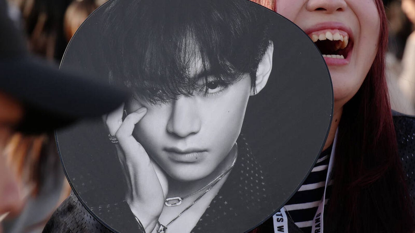 A smiling fan holding a circular hand fan featuring a portrait of BTS member V