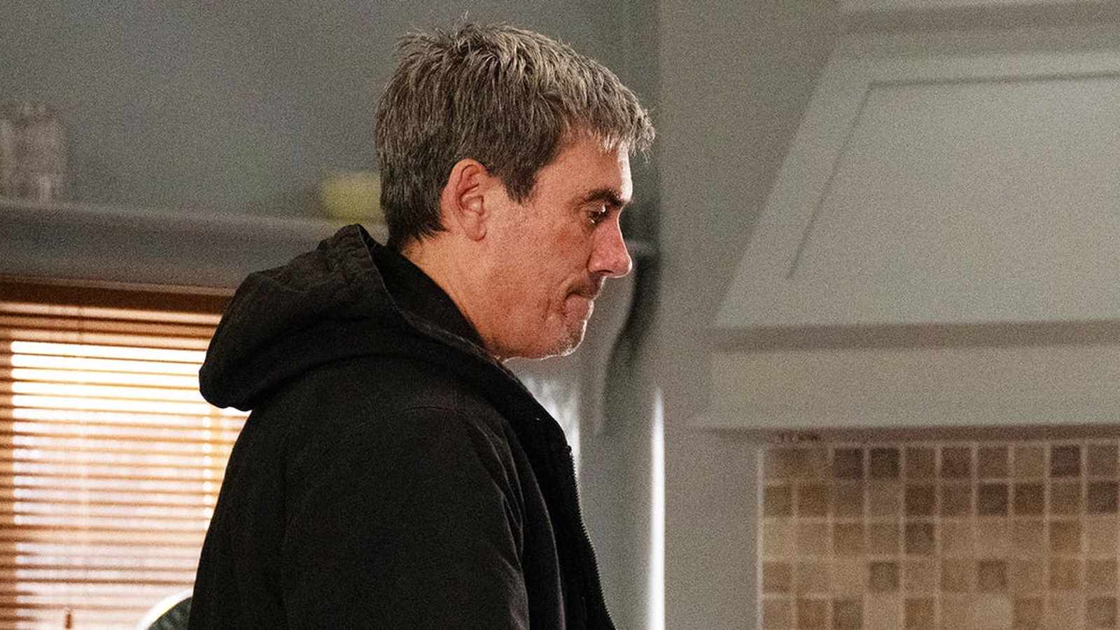 Cain Dingle looking serious while wearing a black hooded jacket in a kitchen