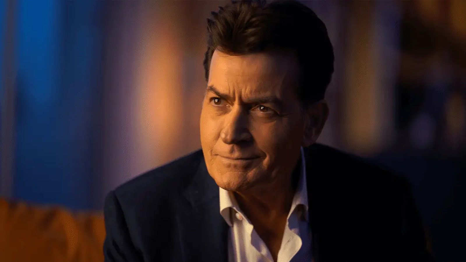 Charlie Sheen looking off-camera with a thoughtful expression in a dark suit jacket