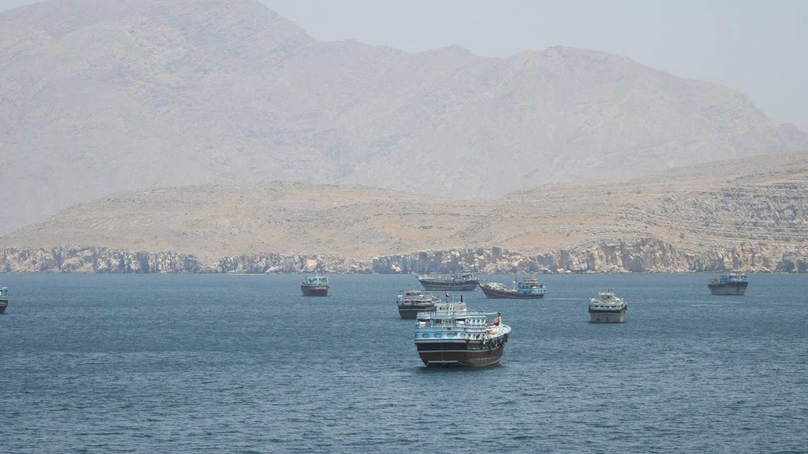 Several traditional wooden dhow boats anchored in the waters of the Strait of Hormuz