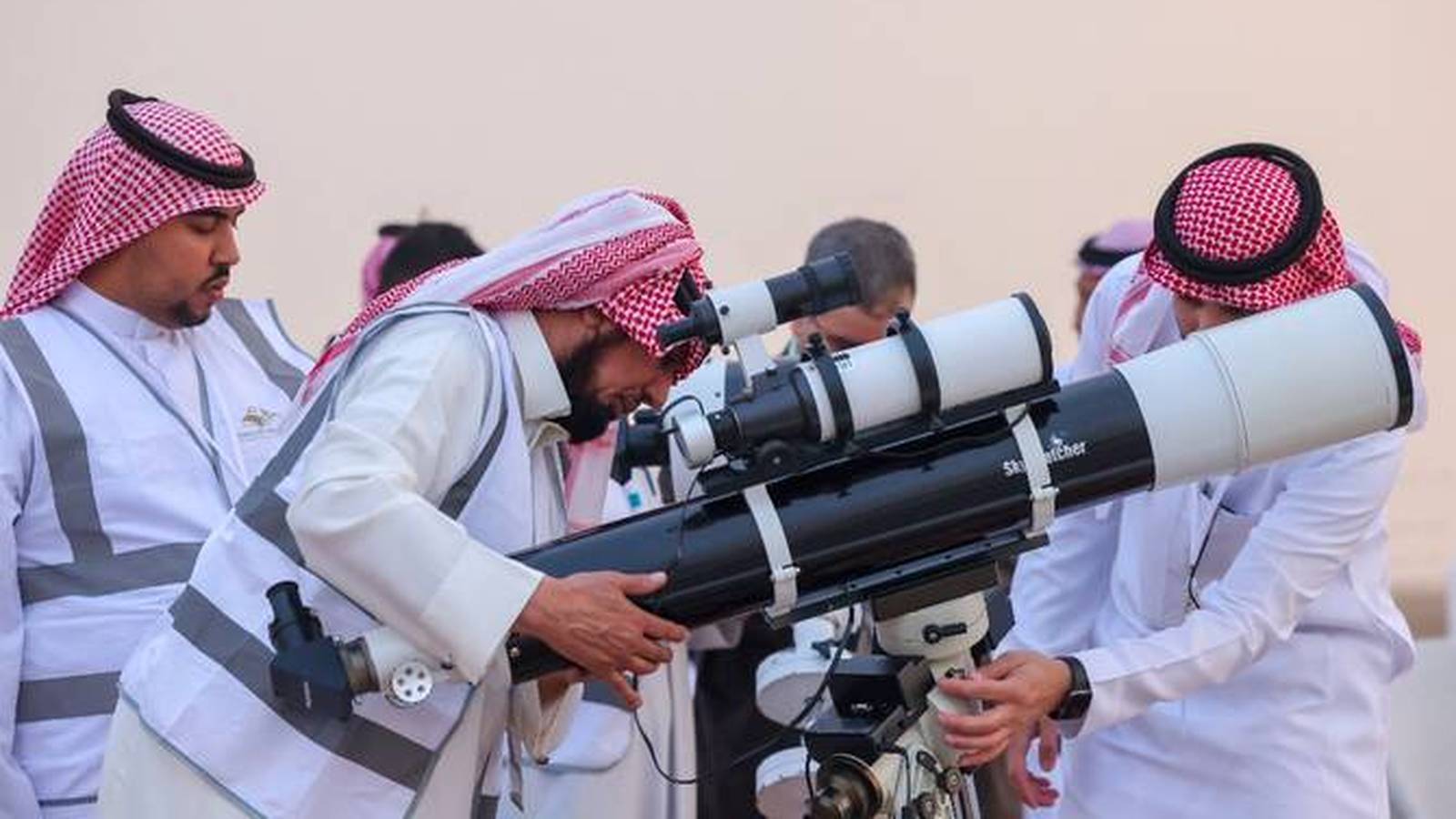 Men in traditional Saudi clothing using telescopes to sight the moon for Dhul Hijjah