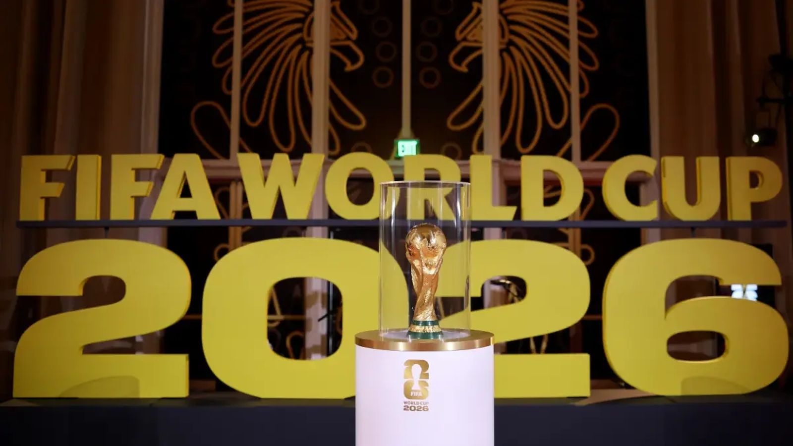 The official FIFA World Cup 2026 trophy displayed on a pedestal with large yellow branding