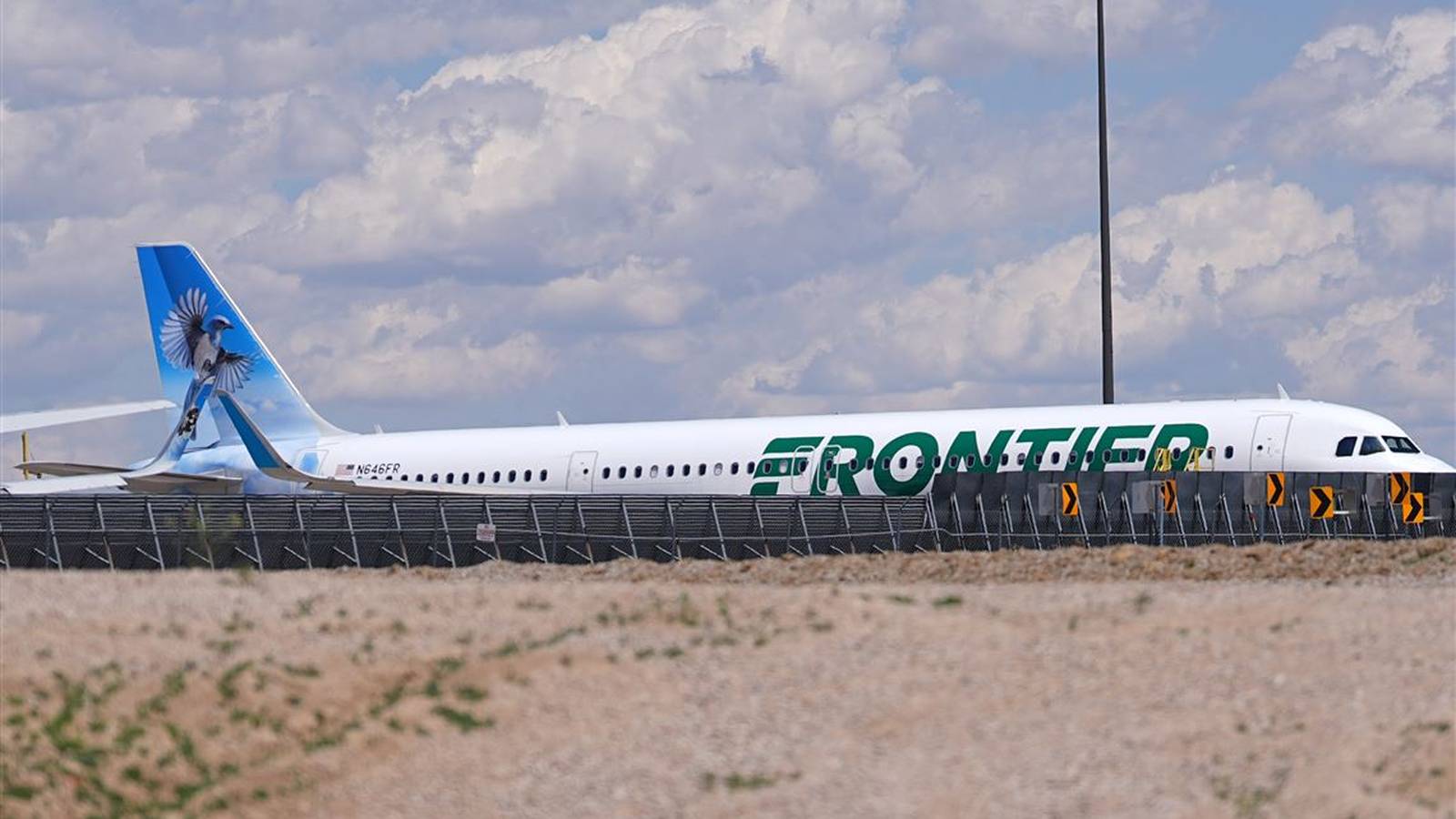 A Frontier Airlines passenger jet parked on the tarmac near a chain link fence