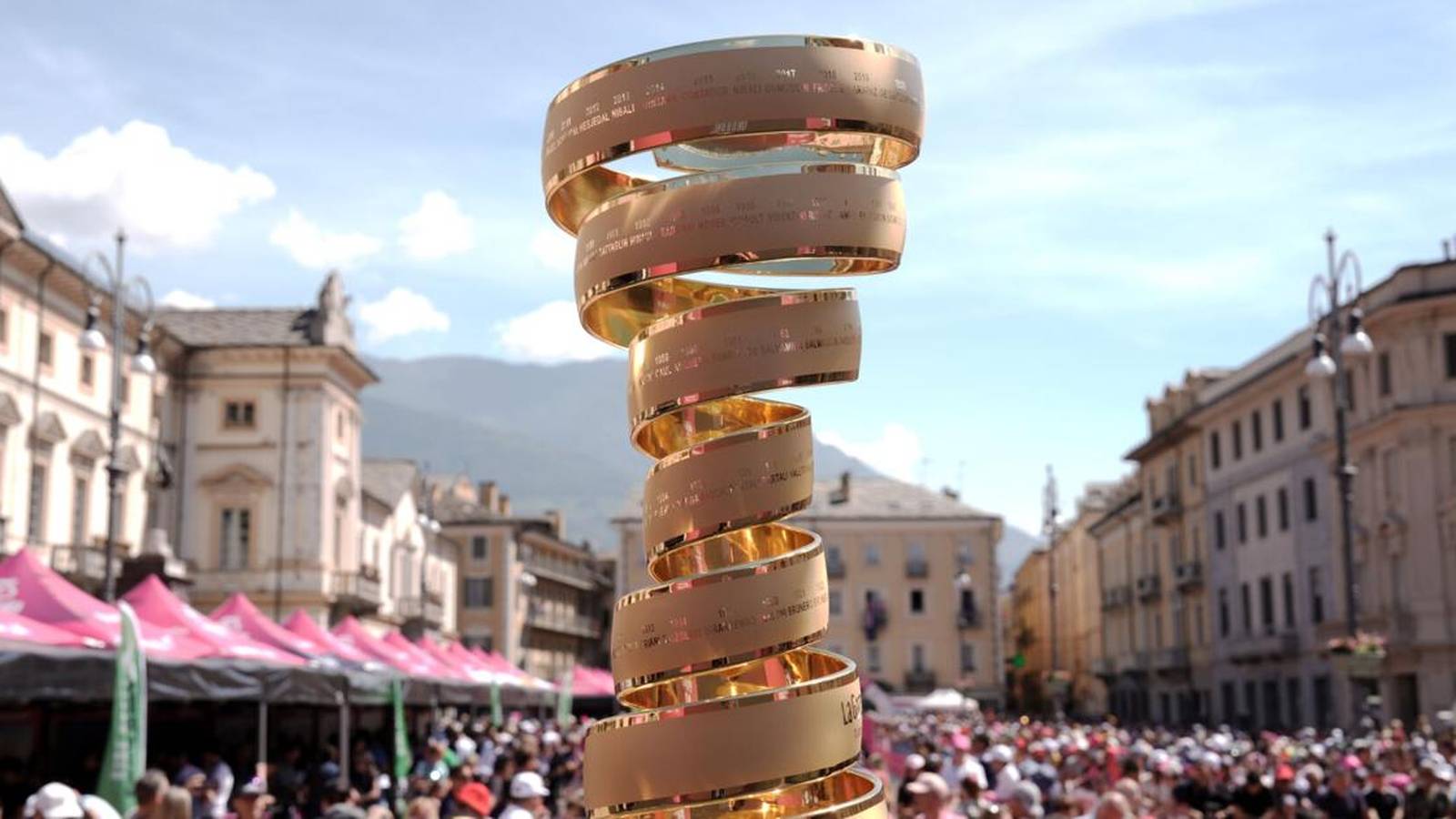 The golden spiral Trofeo Senza Fine trophy displayed in a crowded Italian town square