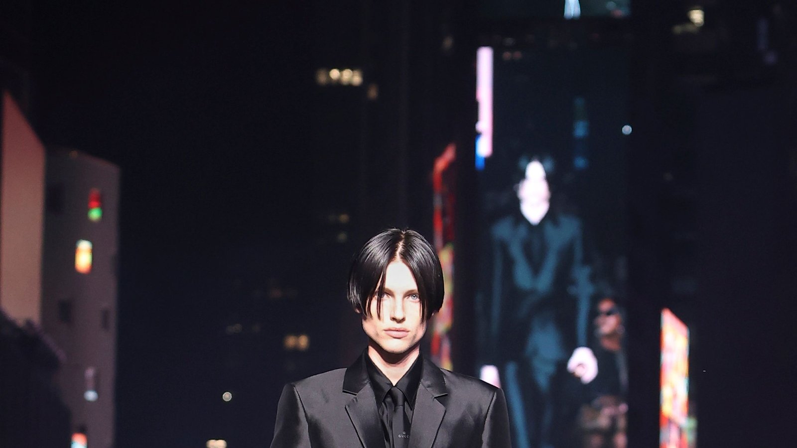 A male model with dark hair wearing a black suit on a runway