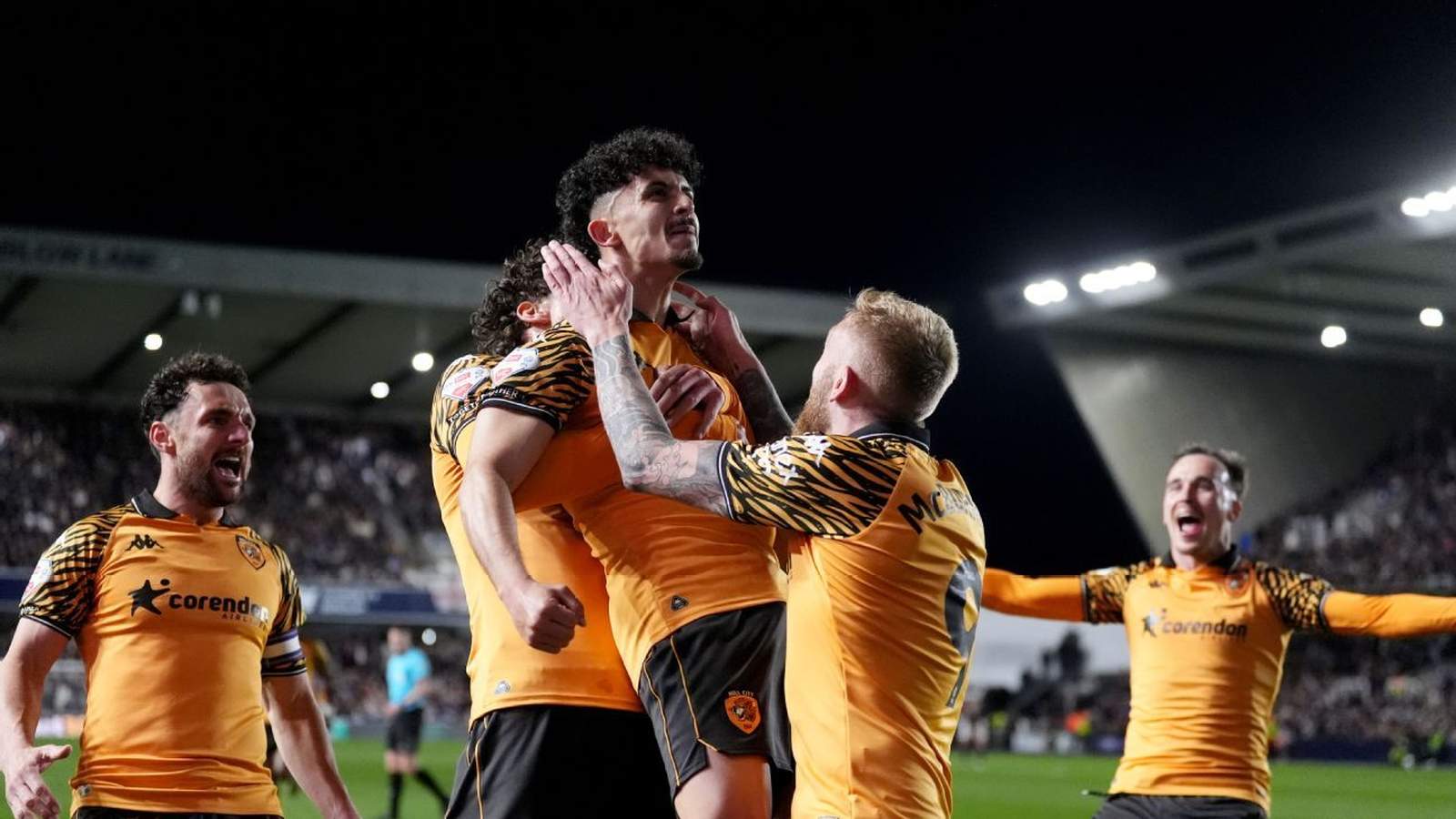Hull City football players in tiger-stripe jerseys celebrating a goal on the pitch