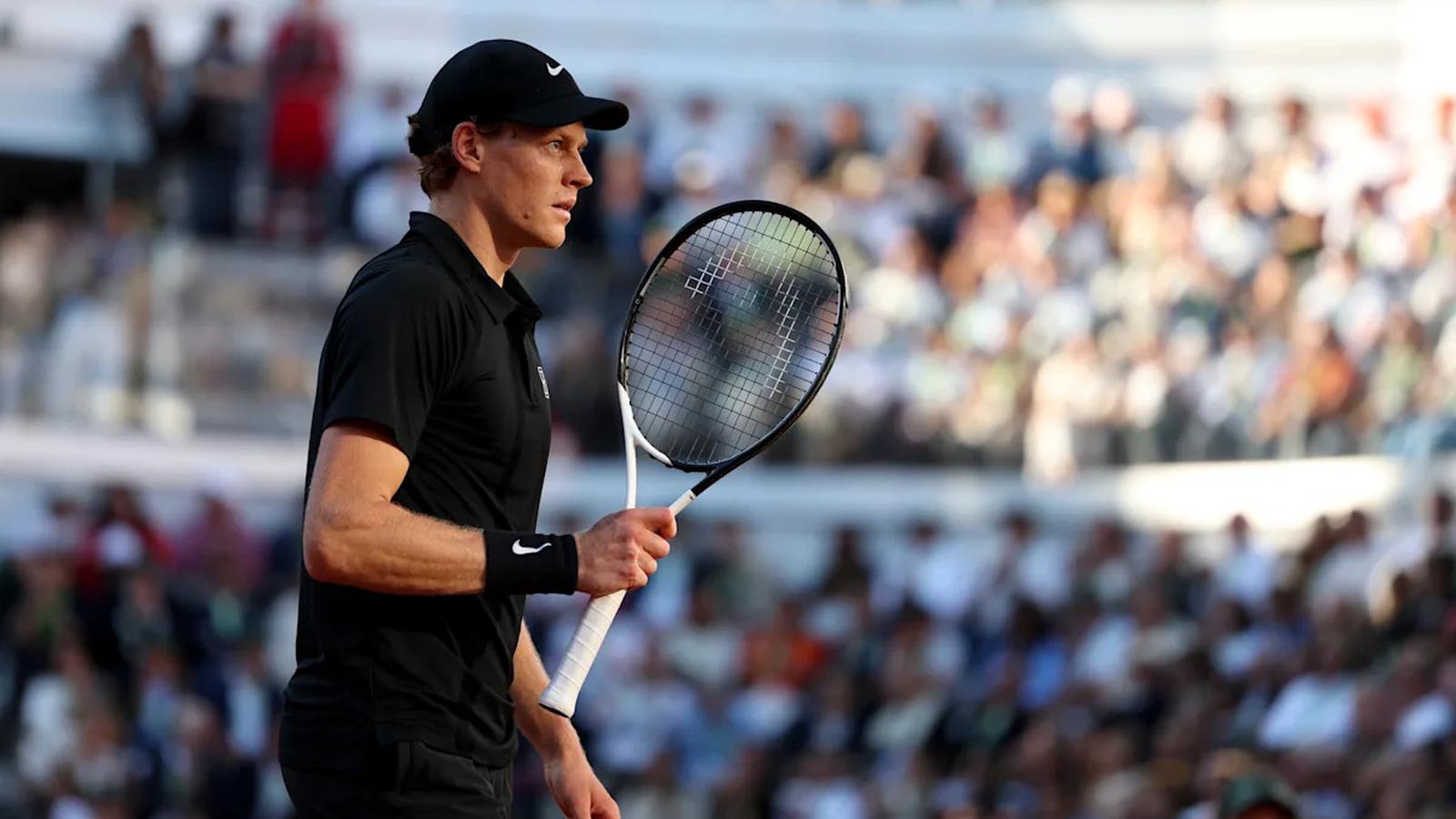 Jannik Sinner wearing a black cap and shirt holding a tennis racket