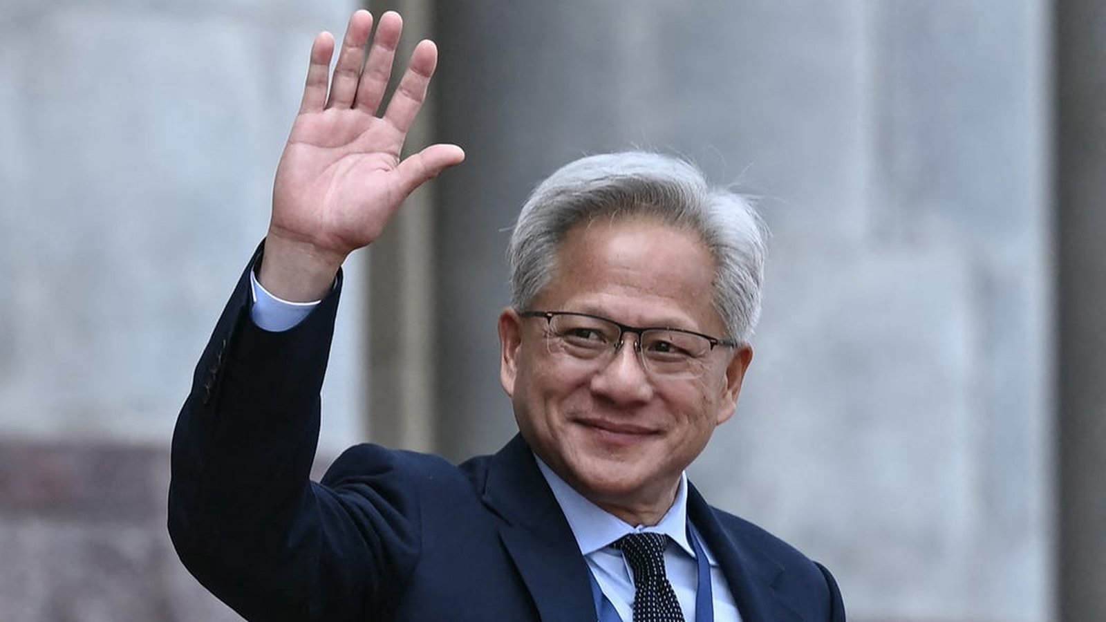Nvidia CEO Jensen Huang smiling and waving his hand in a formal suit