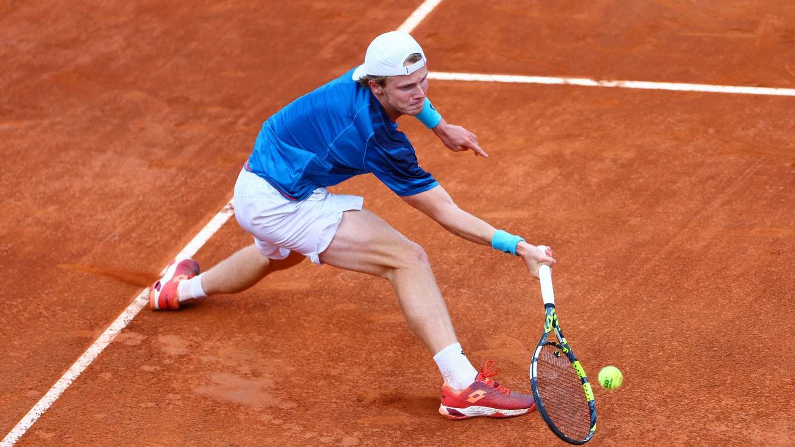 Jesper De Jong lunging to hit a tennis ball on a clay court
