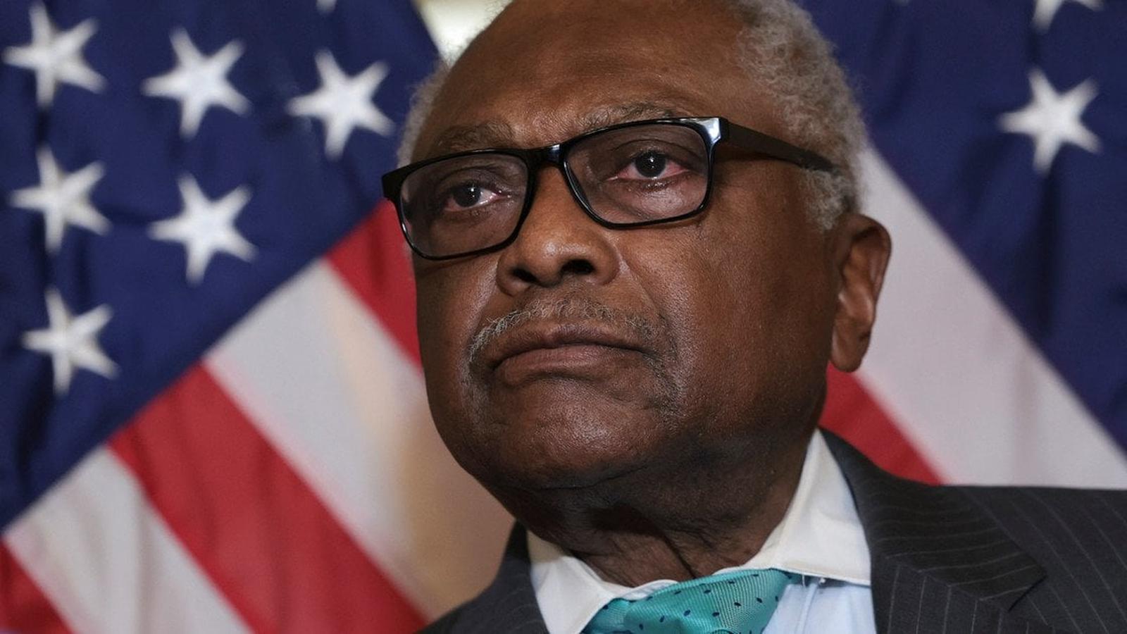 Representative Jim Clyburn wearing glasses and a suit in front of American flags