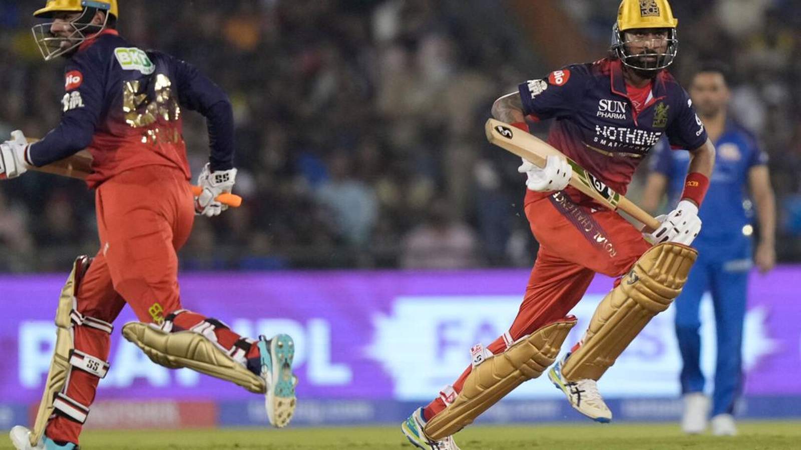 Jitesh Sharma running with a cricket bat during an IPL match, wearing red and blue uniform